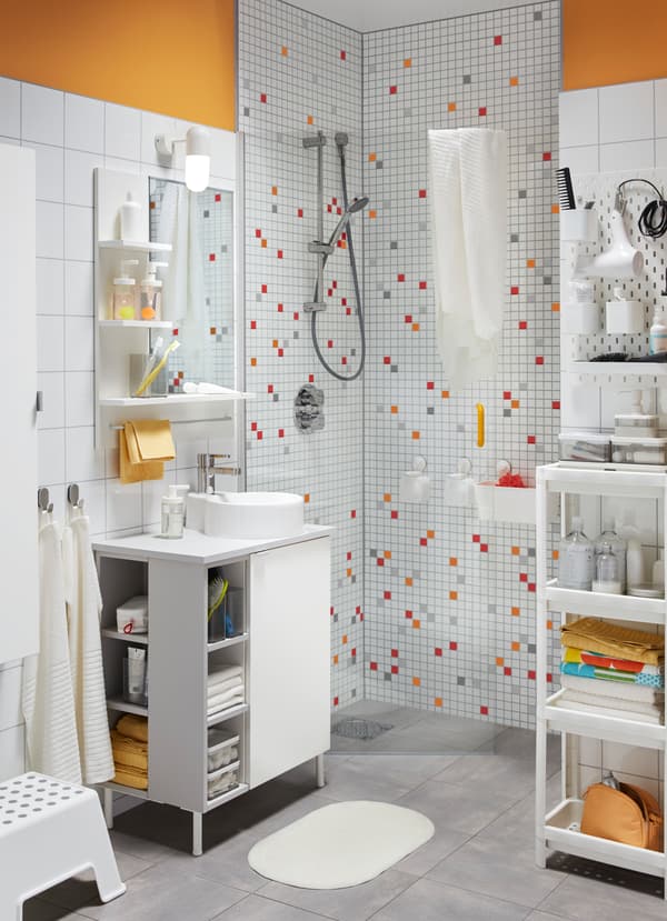 A light bathroom with colorful shower tile, a white sink cabinet, and shelving with various bathroom accessories.