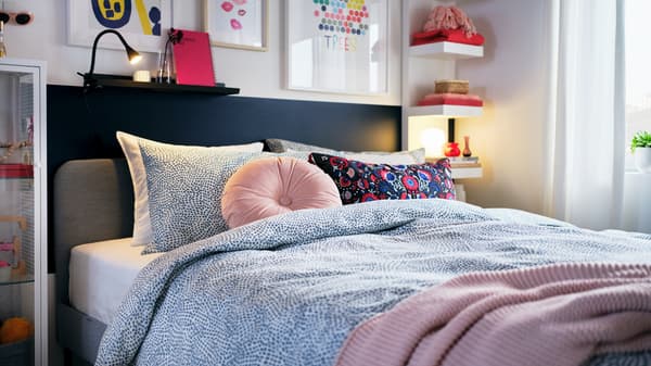 A light bedroom with colourful decorations, a light-grey SLATTUM bed made with blue-and-white TRÄDKRASSULA bed linen.