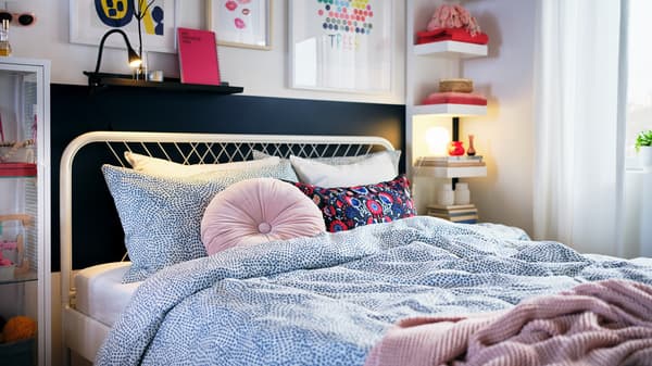 A light bedroom with colourful decorations and a white NESTTUN bed made with blue-and-white TRÄDKRASSULA bed linen.