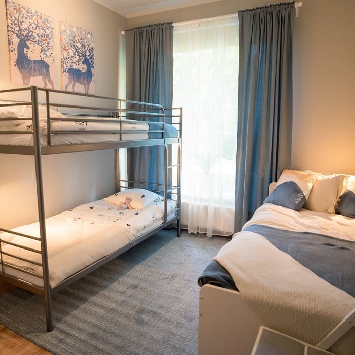 A light beige and grey-toned room with a bunk bed on one wall and a neatly made bed on the opposite side.