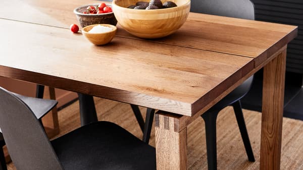 A light brown MÖRBYLÅNGA wooden table with natural oak grain and colour variations, matched with dark modern chairs.
