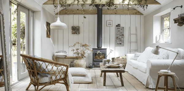 A light-coloured living room with a white sofa, wicker chair, wooden beams and floorboards.