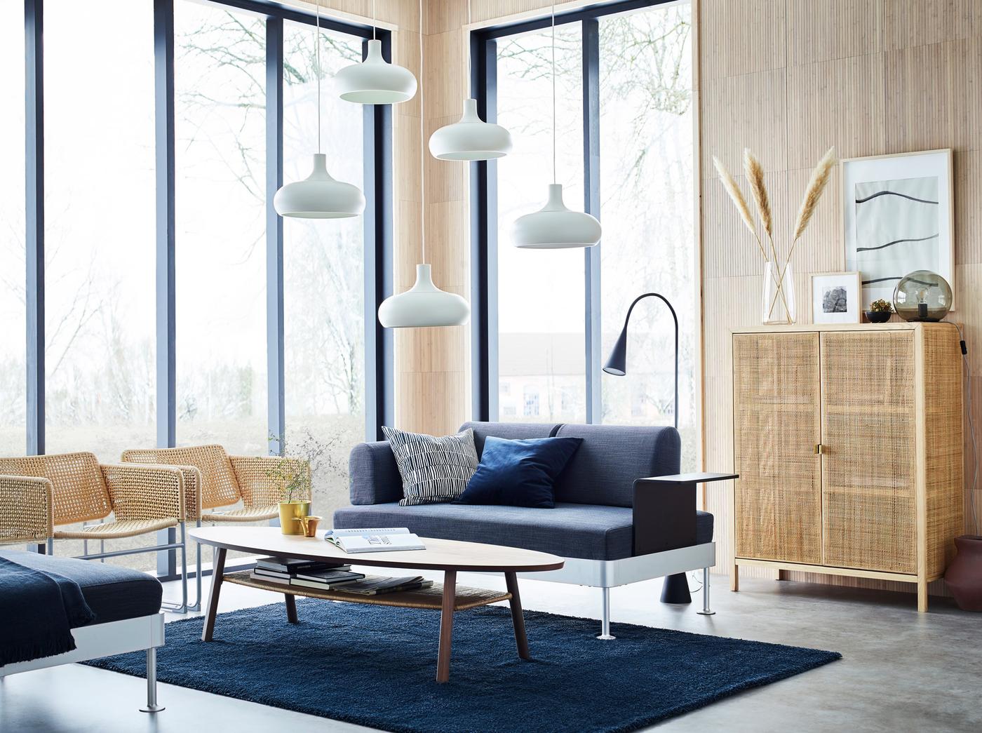 A light-filled beige, blue and grey living room with large windows and a DELAKTIG 2-seat sofa in anthracite with side table.