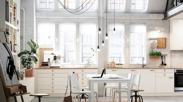 A light-filled open kitchen in a loft with two rows of cabinets with white VEDDINGE doors and a white table and chairs.