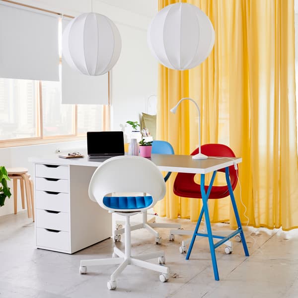 A light gray/white table with blue legs and drawer unit, white round pendant lamps, three swivel chairs and yellow curtains.
