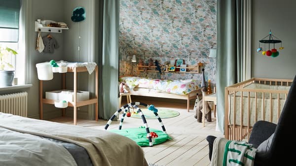 A light green bedroom containing a double bed and SNIGLAR cot, bed and changing table, with a KLAPPA baby gym on the floor.