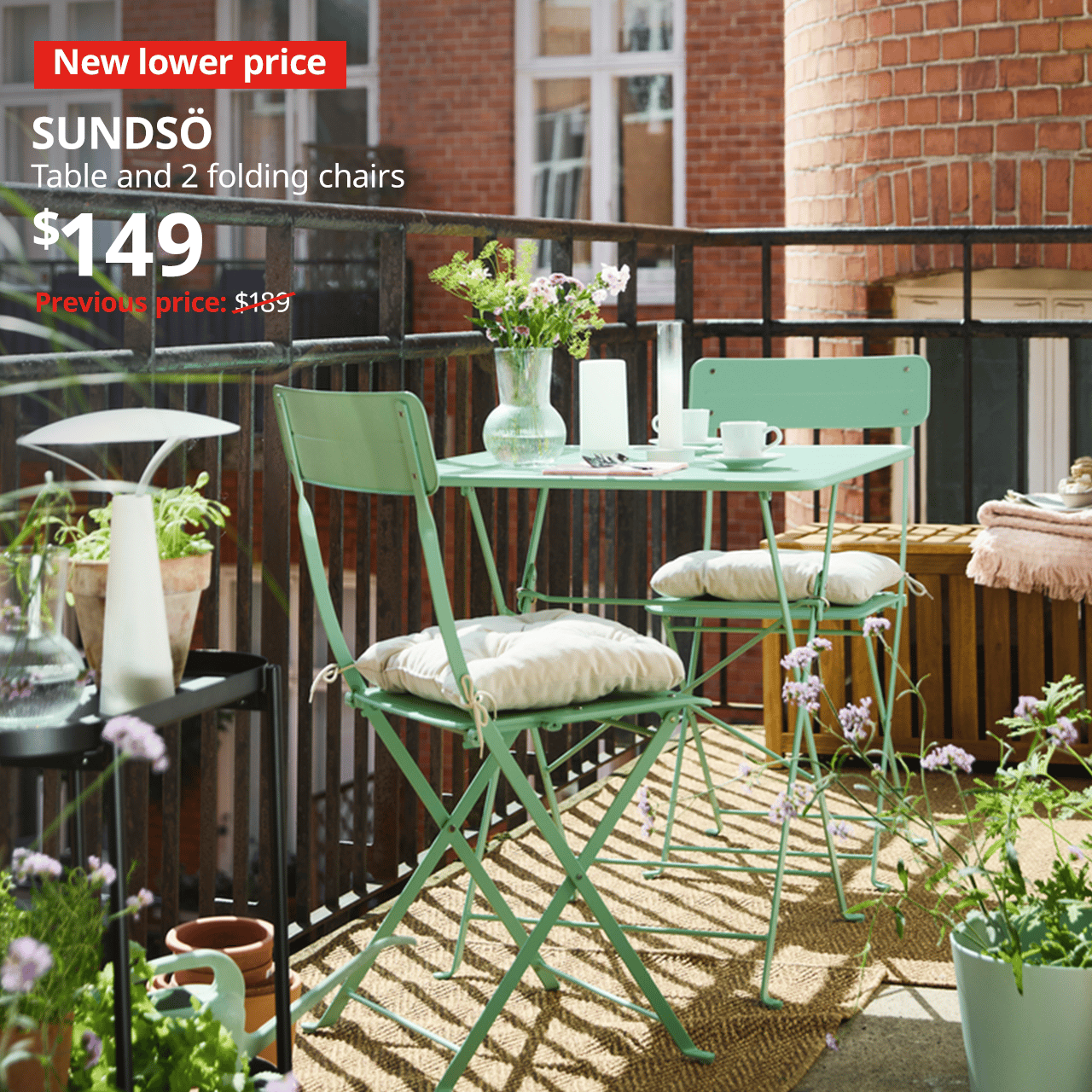 A light green SUNDSO outdoor table and two chairs in a balcony area, with plants. A red "New lower price" label is on the top left of the image with white text that reads: SUNDSO, table and 2 folding chairs, Price at $149, Previous price, $189.