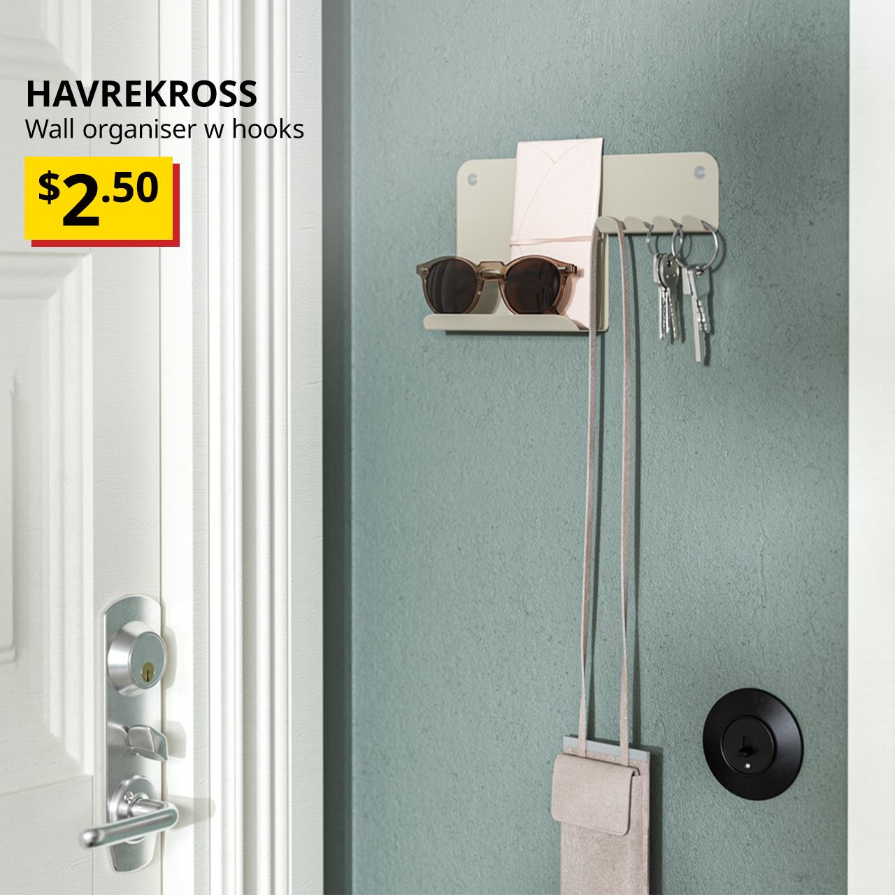 A light grey-beige HAVREKROSS wall organiser with hooks is positioned next to the door with sunglasses placed on the shelve space and keys on the hooks. Text on the top left of the image reads: HAVREKROSS, wall organiser with hooks. Price: $2.50. 