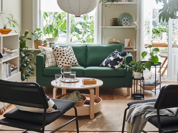 A light living room dominated by a dark-green PÄRUP two-seat sofa, graphic-pattern textiles, wood accents and leafy plants.