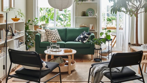 A light living room dominated by a dark-green PÄRUP two-seat sofa, graphic-pattern textiles, wood accents and leafy plants.