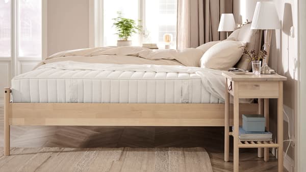 A light neutral-styled bedroom with a bed and a white mattress exposed on the side.