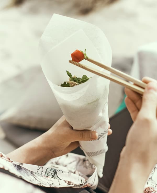 A light noodle meal is eaten with chopsticks out of a parchment paper cone.