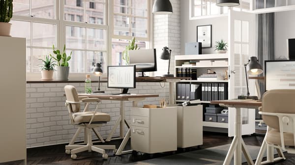 A light office with facing workspaces. An ALEFJÄLL office chair stands next to IDÅSEN sit-stand desks and drawer units.