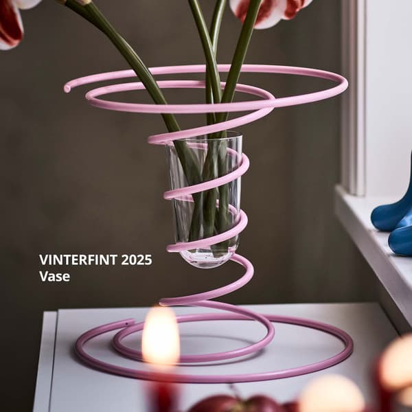 A light pink VINTERFINT 2025 spiral vase with a bunch of flowers, placed beside a light blue VINTERFINT candlestick 