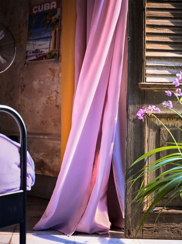 A light purple, air purifying curtain blowing in the wind next to a wooden shutter.