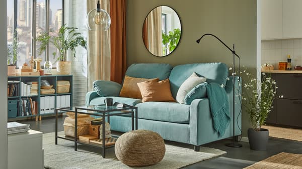 A light turquoise sofa with high back, nesting tables, gray-turquoise open cabinets by the window with books, baskets and files.