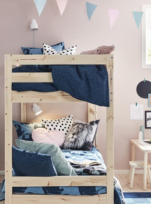 A light wood bunk bed in a child’s bedroom with blue bedding and pink walls.