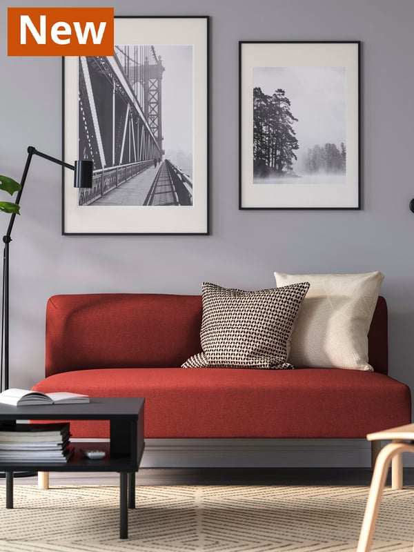 A LILLEHEM two-seater sofa in Tonerud red with two cushions. Two black RÖDALM frames with black and white art posters hang behind the sofa on the wall.