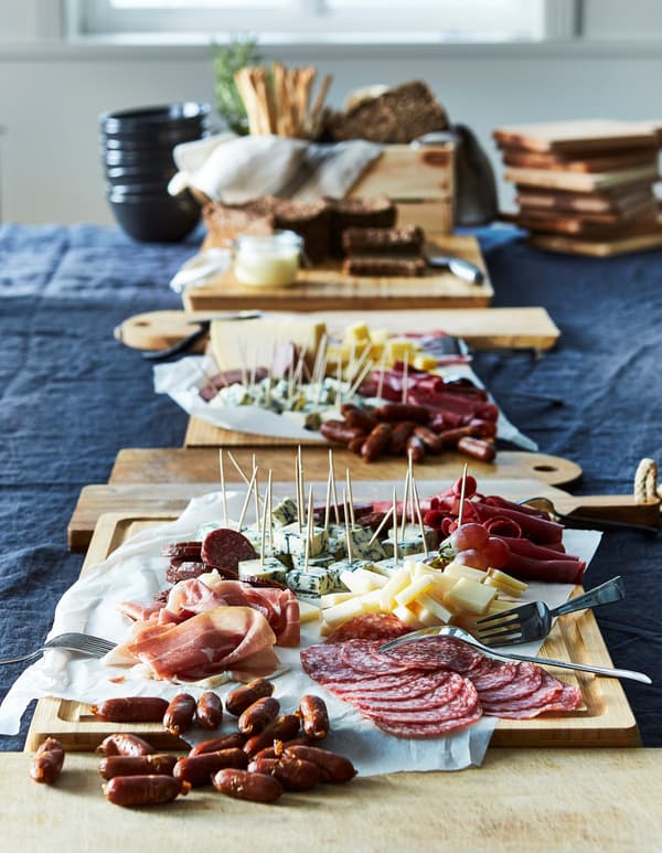 A line of chopping boards covered in a variety of meats and cheeses on a dining table.