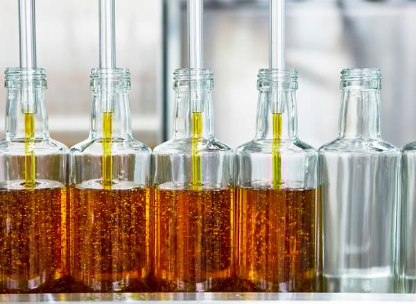 A lineup of glass bottle being filled at a factory with canola oil.