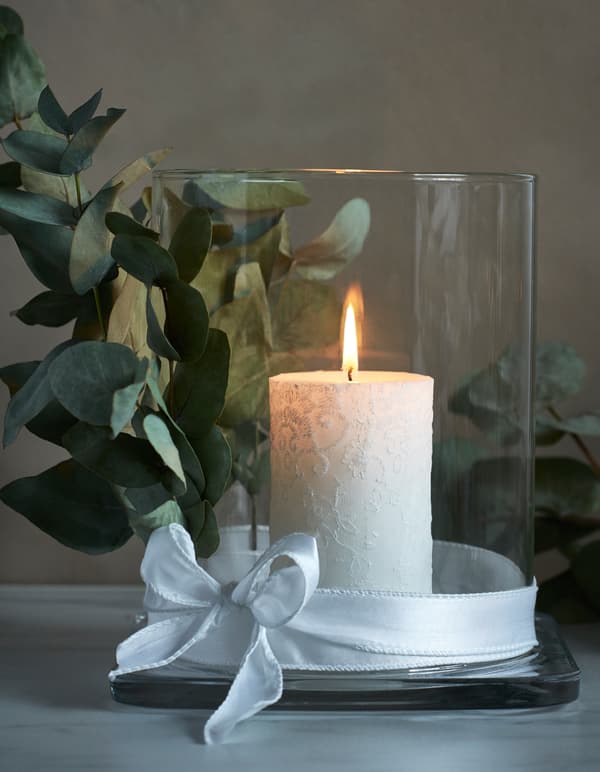 A lit candle is displayed in a glass lantern tied with a ribbon.