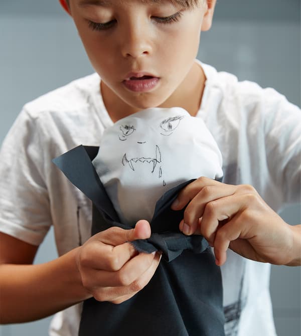 A little boy ties a black cape around his DIY Dracula.