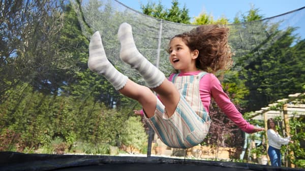 A little girl bounces up and down from a sitting position on a trampoline.