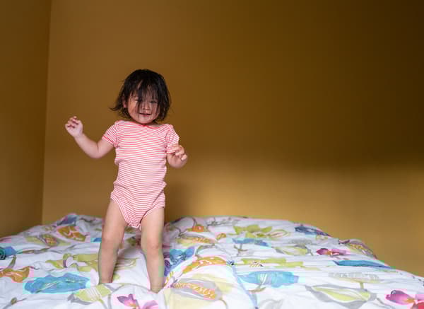 A little girl with dark hair all over her face is happily jumping on a bed.