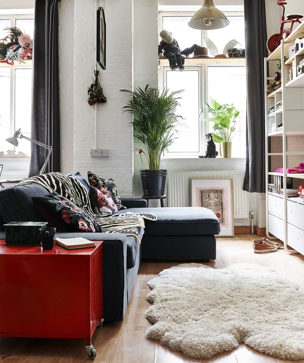 A living area with dark blue L-shaped sofa, sheepskin rug and painted brick walls.