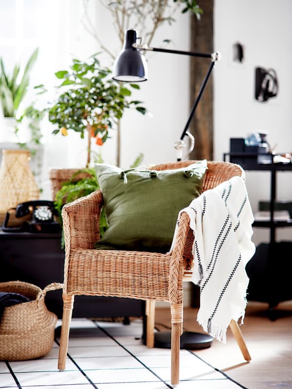 A living room area in black, white and green with large plants, an AGEN rattan chair and accents in natural materials.