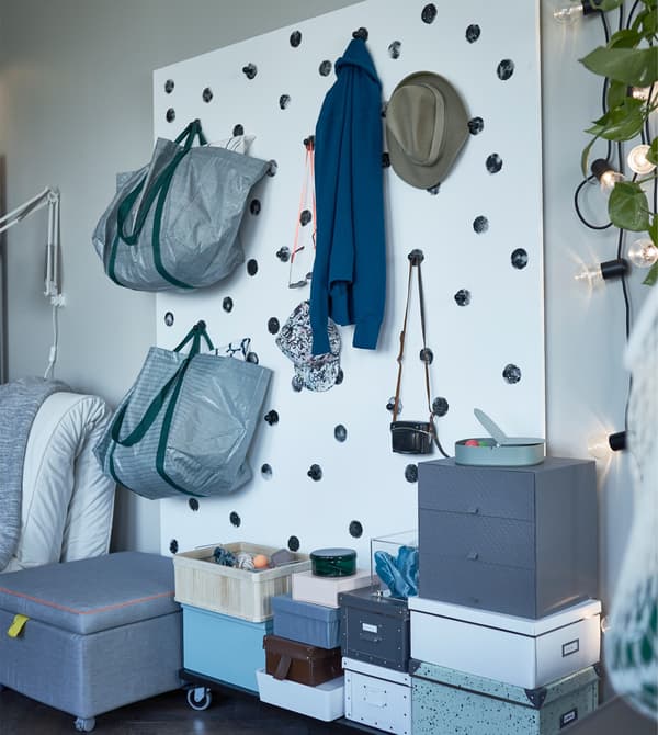 A living room storage wall created with hooks for hanging clothes and bags and storage boxes stacked on the floor.