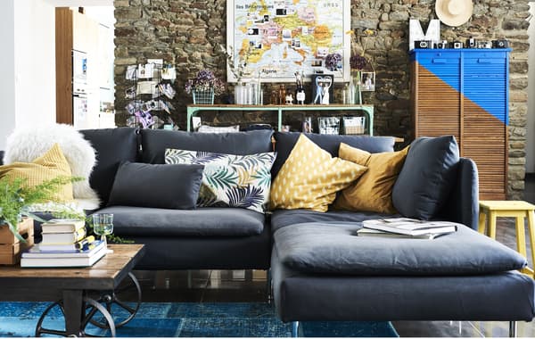 A living room with a grey sofa section with chaise lounge and colourful cushioned textiles.