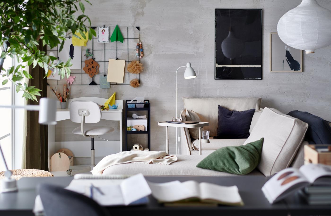 A living room with a small workstation in a corner, a laptop stand by an armchair with cushions and a chaise longue.