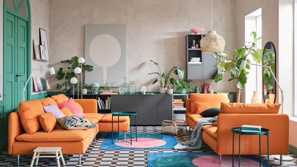 A living room with a sofa and chaise lounges in orange, a cabinet combination in gray, colorful rugs and green tray tables.