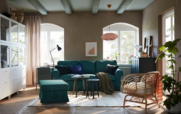 A living room with a sofa and footstool in dark turquoise, a white storage combination and a dark blue-green cabinet.