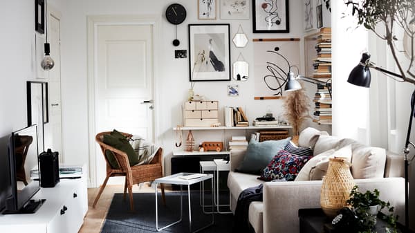 A living room with a sofa-bed, a rattan/bamboo chair, a TV bench, a dark gray rug, a black wall clock and black lamps.