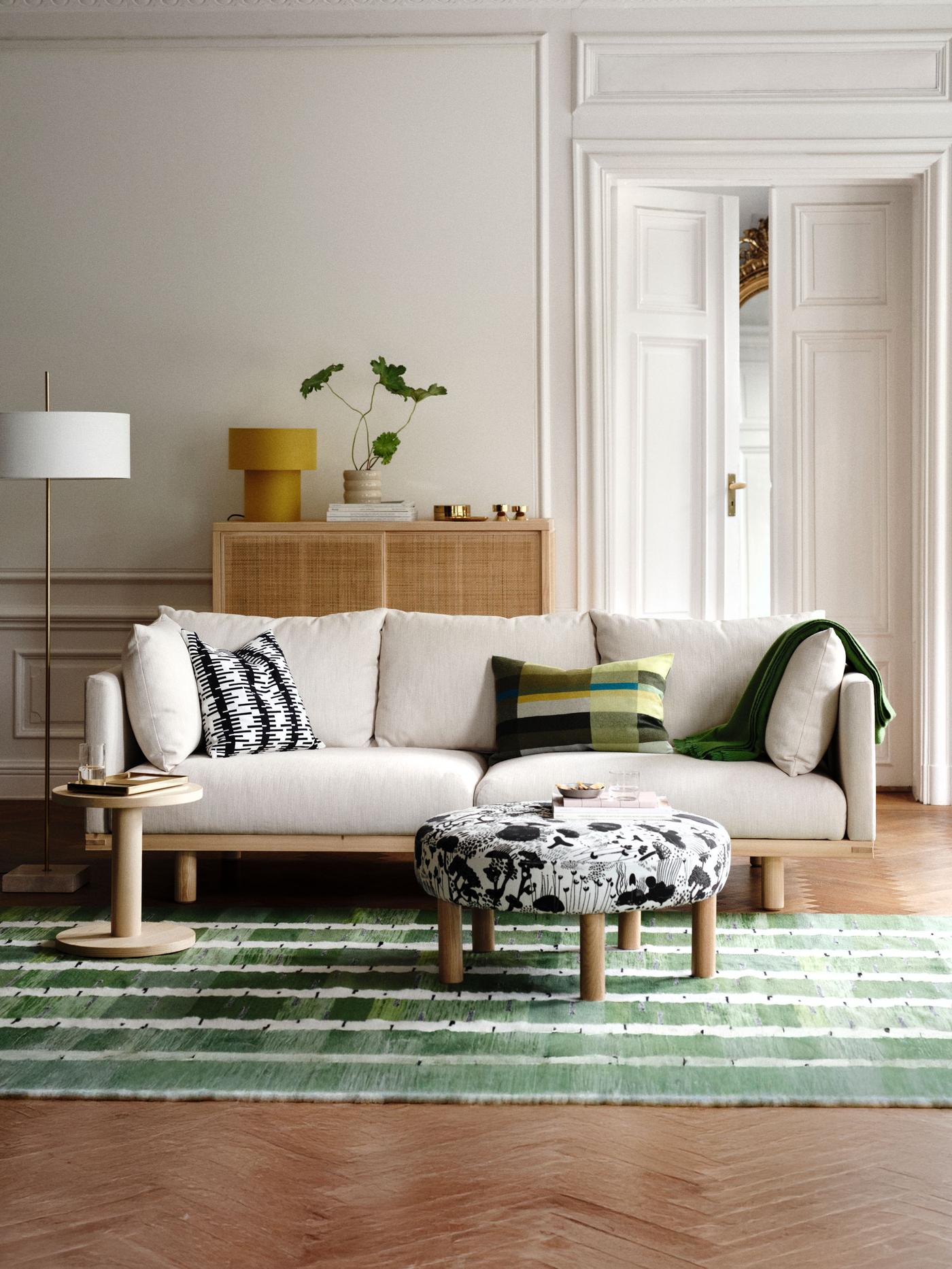 A living room with a STOCKHOLM 2025 3-seat sofa, pillows and a throw resting on it, side table and pouffe on a rug in front.