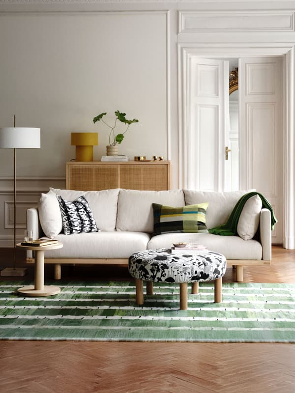 A living room with a STOCKHOLM 2025 3-seat sofa, pillows and a throw resting on it, side table and pouffe on a rug in front.