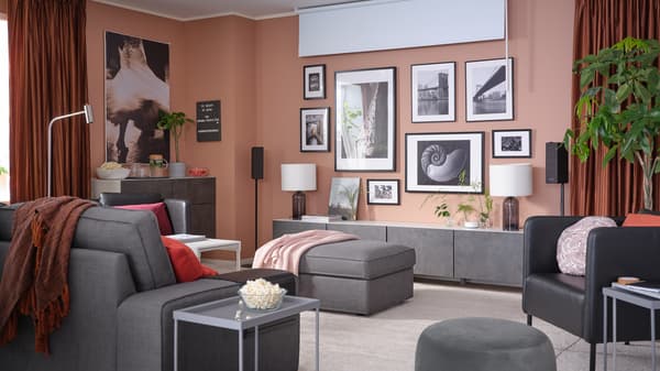 A living room with a wall of framed artworks, a block-out roller blind, room darkening curtains and a 3-seat sofa.