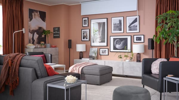A living room with a wall of framed artworks, a block-out roller blind, room darkening curtains and a 3-seat sofa.
