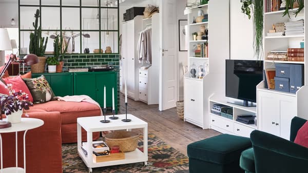 A living room with a wing chair and footstool in dark green, green cabinets and a white HAUGA TV/storage combination.