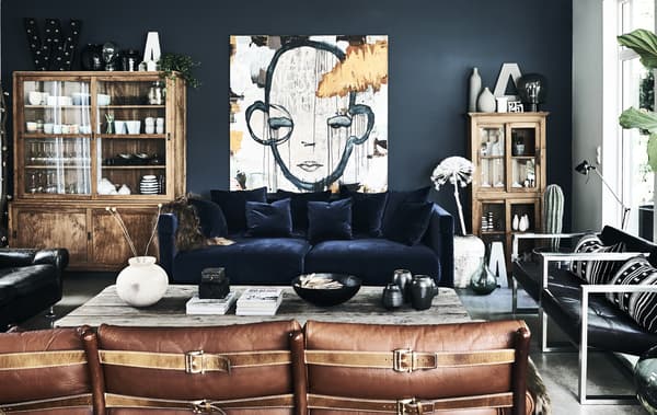A living room with blue velvet sofa and dark walls.