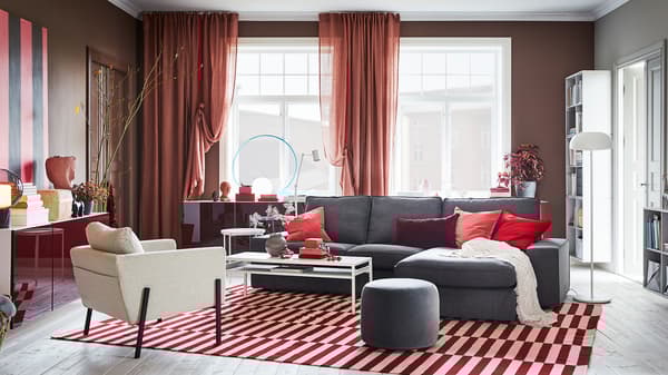 A living room with brown-pink curtains, a red/white rug, a grey sofa and wall-mounted cabinets with red high-gloss doors.