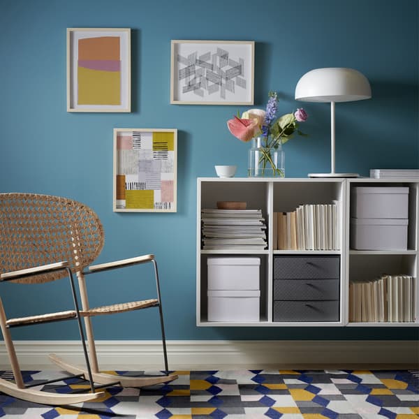 A living room with cubed open storage unit on the wall and a rattan rocking chair.