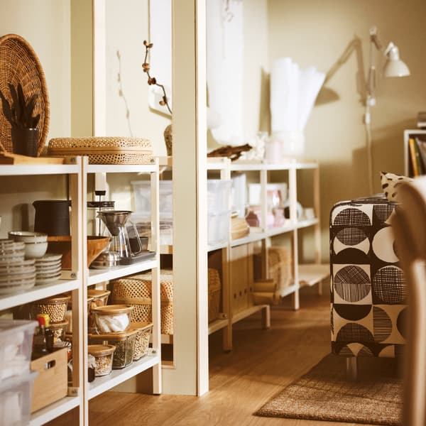 A living room with EKENABBEN open shelving units containing GLADELIG bowls, a HÖGMODIG coffee maker and boxes with lids.