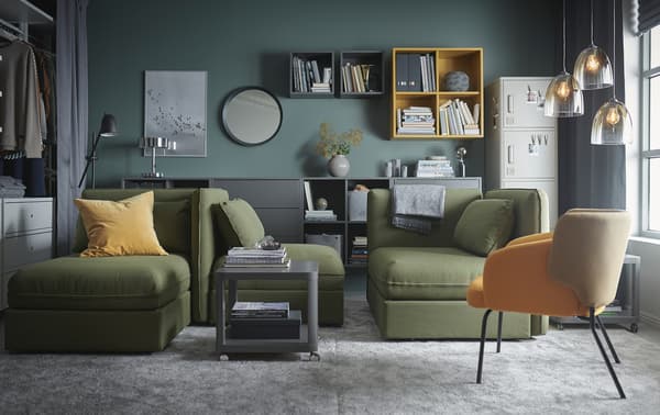 A living room with green VALLENTUNA modular sofa-beds, grey large rugs, grey and yellow cabinets and glass pendant lamps.