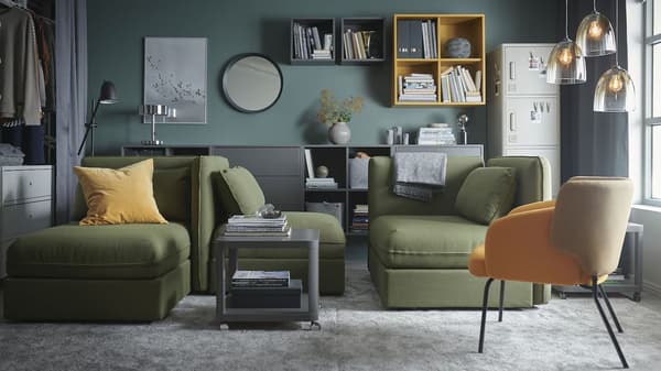 A living room with green VALLENTUNA modular sofa-beds, grey large rugs, grey and yellow cabinets and glass pendant lamps.