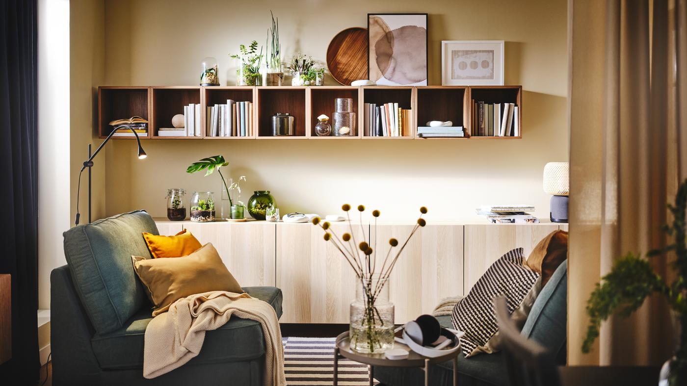 A living room with KIVIK armchairs facing each other. EKET shelving storage with books is mounted in a line across the wall.