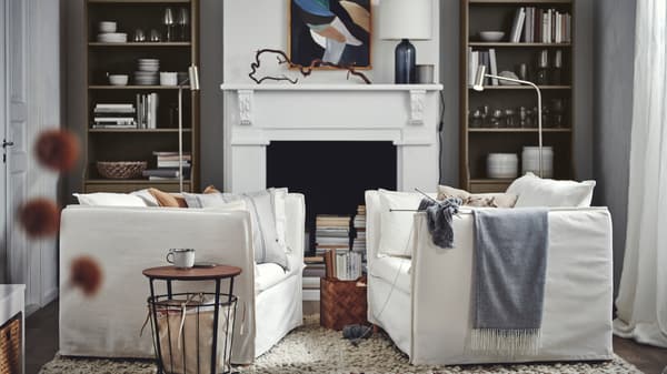A living room with two facing white BACKSÄLEN armchairs against a backdrop of beige HAUGA high cabinets framing a fireplace.