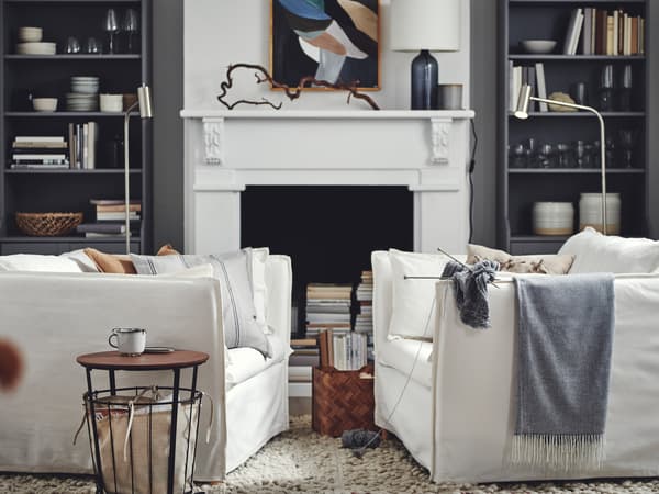 A living room with two facing white BACKSÄLEN armchairs against a backdrop of grey HAUGA high cabinets framing a fireplace.